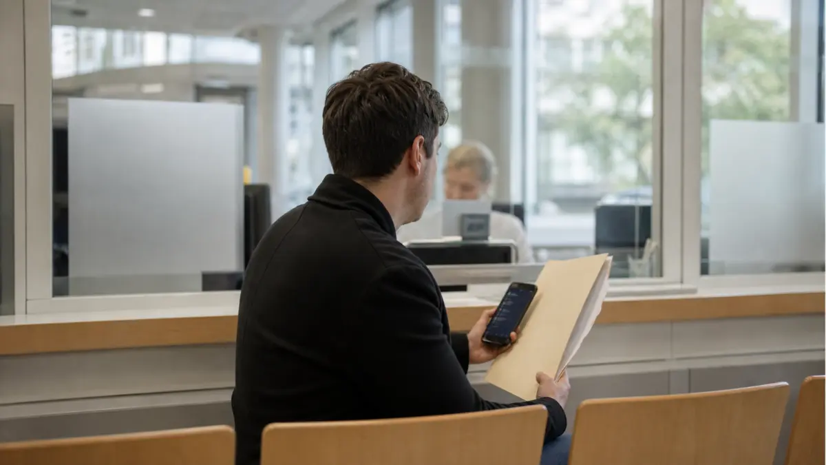 Anonymer Krypto-Anleger mit Unterlagen und Smartphone am Schalter eines Finanzamts